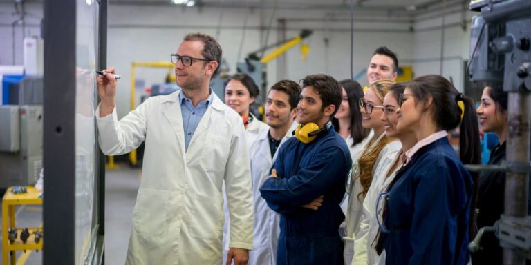 a-small-group-of-engineering-students-standing-in-a-workshop-as-they-watch-their-professor-write-a-l.jpeg